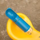 A portable blue pet water bottle with an attached trough sits on a yellow curved surface outdoors. The bottle has a transparent base.