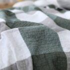 Close-up of a crumpled fabric with a checkered pattern in green and white shades. The texture of the material is visible, and the colors create a relaxed, cozy appearance.