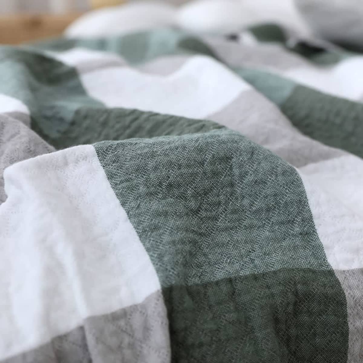 Close-up of a crumpled fabric with a checkered pattern in green and white shades. The texture of the material is visible, and the colors create a relaxed, cozy appearance.