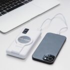 Laptop on a desk with a white power bank labeled THE COVE charging a smartphone via a cable.