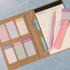 An open planner with pastel sticky notes labeled for each day of the week and weekend. A lined notepad with a date section is on the right, alongside a pink highlighter and a purple pen. The background is a geometric, blue pattern.