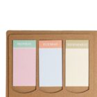 A brown notepad with three labeled sections for Monday, Tuesday, and Wednesday. Each section features a colored sticky note: pink for Monday, blue for Tuesday, and yellow for Wednesday.
