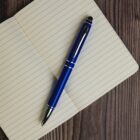 A blue and black pen rests diagonally on an open lined notebook, placed on a wooden surface.