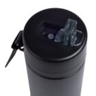A close-up of the top of a black thermos bottle with a flip-open lid, showing the transparent mouthpiece and carrying handle. The lid is closed, and the smooth black surface of the thermos is visible.