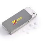 A rectangular metallic tin labeled Energy Boost with a yellow and red design is open, revealing small white tablets inside. Several tablets are scattered outside on a white surface.