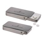 Two metal tablet holders with sliding lids, engraved with Old Deer Lodge and a deer logo. One is open revealing white tablets inside, and the other is closed.