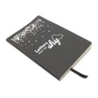 A notebook with a black cover titled Letters from the Sky. The cover features scattered white letters and a cloud design. A black ribbon bookmark is attached. The notebook is angled and shown on a plain white background.