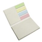 An open notebook showing a blank page on one side and four colored sticky notes—green, yellow, blue, and pink—on the other side.
