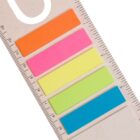 A set of colorful sticky notes in orange, pink, yellow, green, and blue arranged vertically beside a ruler. The ruler is placed on a light beige textured background.