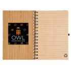 An open spiral notebook with a bamboo cover. The left page features the OWL Scholastic Tutorial Center logo, with an owl and books. The right page is lined, with a recycle symbol at the bottom.