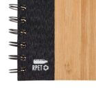 Close-up view of a notebook with a bamboo cover and spiral binding on the left. The binding is black and features a recycling symbol and the text RPET with an icon of a bottle, indicating the use of recycled materials.