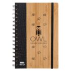 A bamboo spiral-bound notebook with a black spine and elastic band. The cover features a stylized owl logo and the text OWL Scholastic Tutorial Center, along with small icons of books.