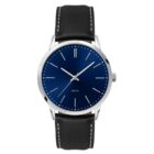 A minimalist wristwatch with a blue dial, silver hour markers, and a black leather strap with white stitching. The watch has a simple design with three hands and no numerals.