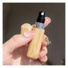 A hand holding a small, cylindrical spray bottle with a wooden finish and a black nozzle. The hand has a pearl ring and a gold bow-shaped ring. The bottle cap is off, revealing the nozzle.