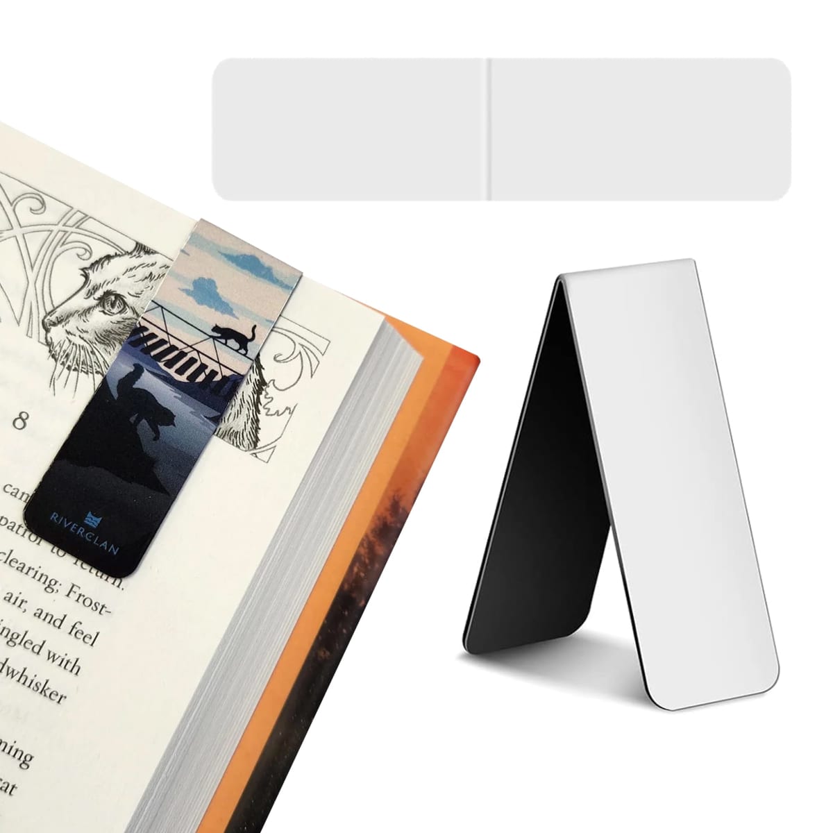 A metallic bookmark with a bird and ladder design is clipped onto an open book. Next to it is a similar bookmark, folded upright, displaying a shiny, reflective surface. Both have RiverClan written on the front.