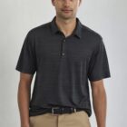 A man wearing a black polo shirt and tan pants stands against a plain background. He has short, curly hair and a neutral expression.