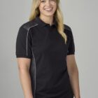A person with long blonde hair smiling while wearing a black polo shirt with white accents. They are standing in front of a plain, light gray background.