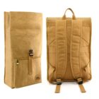 Two tan backpacks displayed side by side. One is upright showing its front with a zipper pocket and buckle closure, while the other is turned around to reveal padded shoulder straps and a top handle. Both have a minimalist, paper-like texture.
