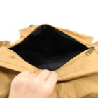 A hand is seen opening a tan leather bag with a zippered main compartment. The interior of the bag is empty and lined with black fabric.