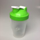 A transparent plastic shaker bottle with a bright green lid and a white flip-top spout, set against a simple gray background.