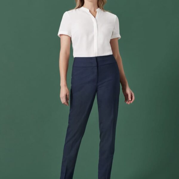 A person is standing against a solid green background wearing a white short-sleeved shirt and dark blue pants. They are wearing black high-heeled shoes and looking forward with a neutral expression.