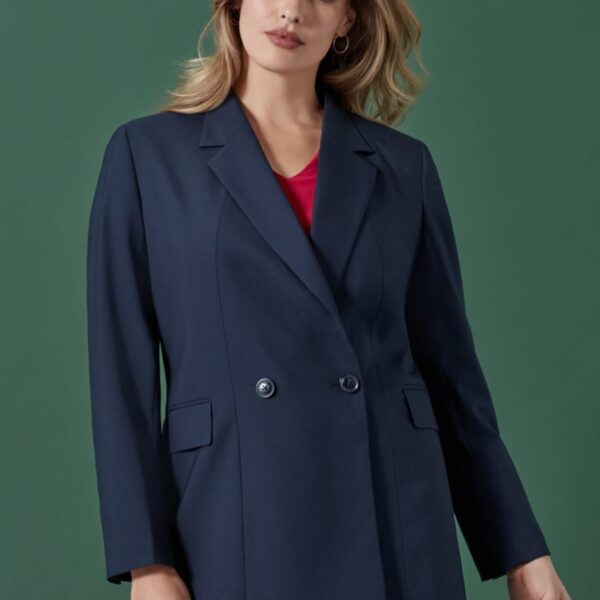 A person with long hair is wearing a navy blue double-breasted suit over a red top, standing against a green background. The individual is looking at the camera with a neutral expression.