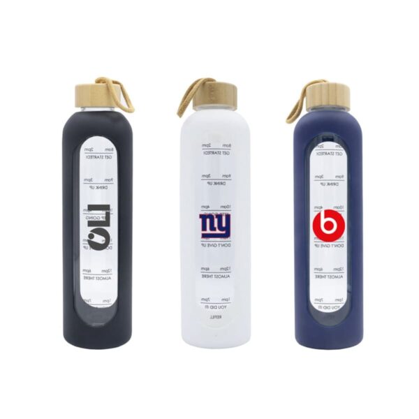Three water bottles with wooden caps and carrying straps are lined up. The bottles have time markers for drinking goals. One bottle is black with a G logo, another is white with a NY logo, and the third is blue with a B logo.