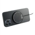 A smartphone with a triple-camera setup, placed face down. A circular wireless charging pad is attached to its back, connected by a cable. The phone has a sleek, dark finish.