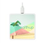 A square wireless charger with a USB connector, featuring an image of beach umbrellas and the text wealthup in stylized font on the top surface. The color scheme includes green, pink, and light blue, with a beach theme.