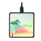 A square wireless charger with a colorful design featuring a sky, beach umbrellas, and the word Wealthup in the center. The charger has a black cable connected at the top.