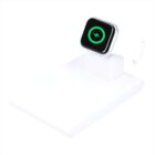 A smartwatch with a white band is placed on a white charging stand. The watch screen displays a green charging symbol. The charging stand is positioned against a plain white background.