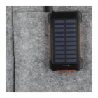A portable solar power bank with a black and orange casing, featuring a solar panel on its surface. It is placed against a gray felt material background.