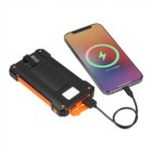 A smartphone displays a charging symbol and 75% Charged while connected to a rugged black and orange power bank via a cable. The power bank features multiple ports and an LED light.