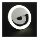 A circular white ring light with a clip attachment, glowing brightly against a dark background. The light is designed for enhancing lighting in photography and video recordings.