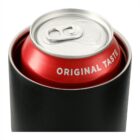 A close-up view of a red soda can with the words Original Taste on it, placed inside a black holder. The cans silver tab is visible on top.