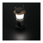 A lantern with a glowing white light is placed on a dark surface. It has a handle on top for carrying and emits a soft illumination around it, creating a focused pool of light on the surface.