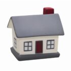 Small model of a house with a gray roof, white walls, gray base, and red features. It has a door and four windows, with a red chimney on top.
