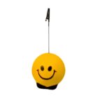 A yellow round object with a smiling face and a small black patch at the bottom. It has a thin vertical rod with a black clip attached at the top, possibly used as a memo holder. The background is plain white.