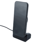 A smartphone resting vertically on a sleek, black charging stand with a connected cable. The phone screen is blank, showcasing the minimalist design of the device and charger against a white background.
