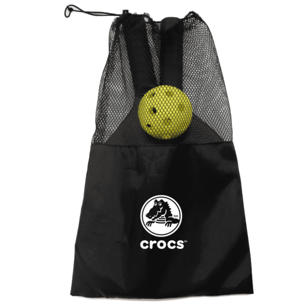 A black drawstring mesh bag with a yellow tennis ball inside. The bag features the Crocs logo, which includes a crocodile silhouette above the brand name crocs in white letters.