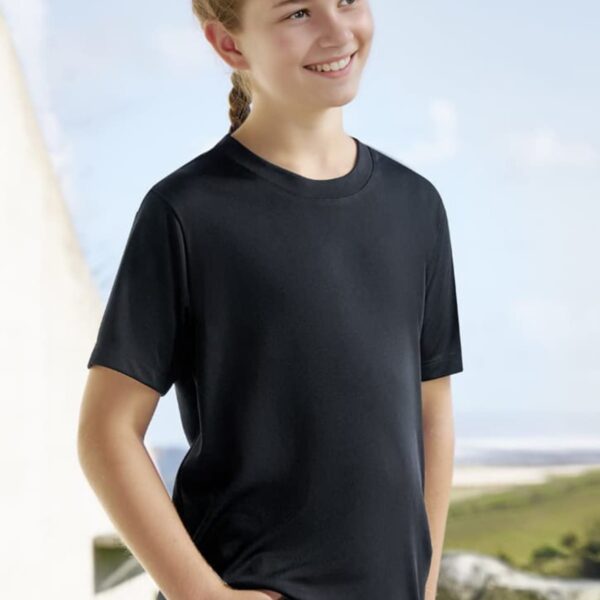 A smiling girl with braided hair is wearing a black T-shirt and blue jeans. She stands outdoors against a backdrop of a blurred landscape with a light blue sky and greenery.