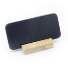 A smartphone in a black case is propped horizontally on a wooden stand. The stand is simple, with a rectangular shape, and the scene is set against a clean, white background.