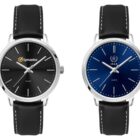 Two wristwatches with black leather straps and silver cases. The left watch has a black dial with the Symantec logo, and the right watch has a blue dial with the IAEA logo. Both have minimalist hour markers and hands.