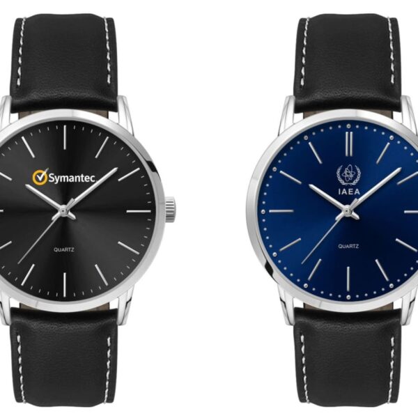 Two wristwatches side by side. The left watch has a black face with the Symantec logo, silver hour markers, and a black leather strap. The right watch has a blue face with the IAEA logo, silver hour markers, and a black leather strap.