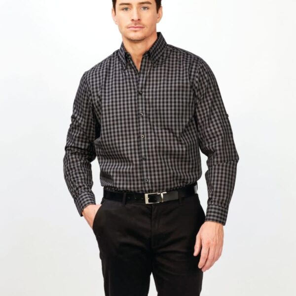 A person standing against a white background, wearing a black and gray checkered button-up shirt and black pants. They have their left hand in their pants pocket and are looking at the camera.