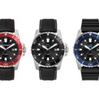 Three diver watches are displayed side by side. The first has a red and black bezel with a perforated strap, the second a black bezel with a smooth strap, and the third a blue and black bezel with a ribbed strap. All feature date displays.