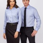 Two people in business attire pose against a white background. The woman wears a light blue blouse and black skirt with a belt, and the man wears a light blue shirt with a black tie and trousers. Both look forward with relaxed expressions.
