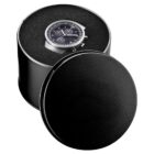 A wristwatch with a black dial and silver case is displayed in a round, black-leather case. The lid is partially open, revealing the watch inside. The case has a soft, textured interior.