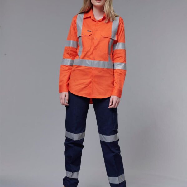 A person wearing an orange high-visibility long-sleeve shirt with reflective stripes and navy pants stands against a gray background. They are also wearing tan work boots.