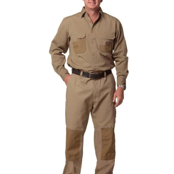 A man in a tan work outfit with pockets on the chest and knees stands smiling. He wears black shoes and a black belt, with his hands relaxed by his sides against a plain white background.